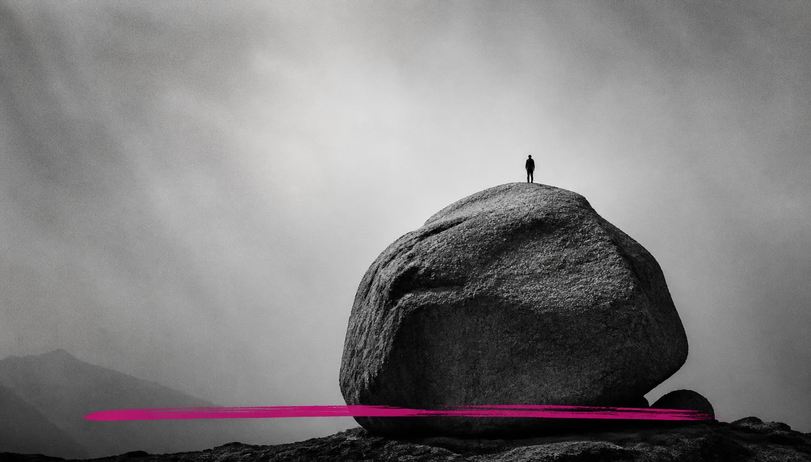 A tiny figure standing atop an enormous boulder in a monochrome landscape, with a single magenta brush stroke across the base.