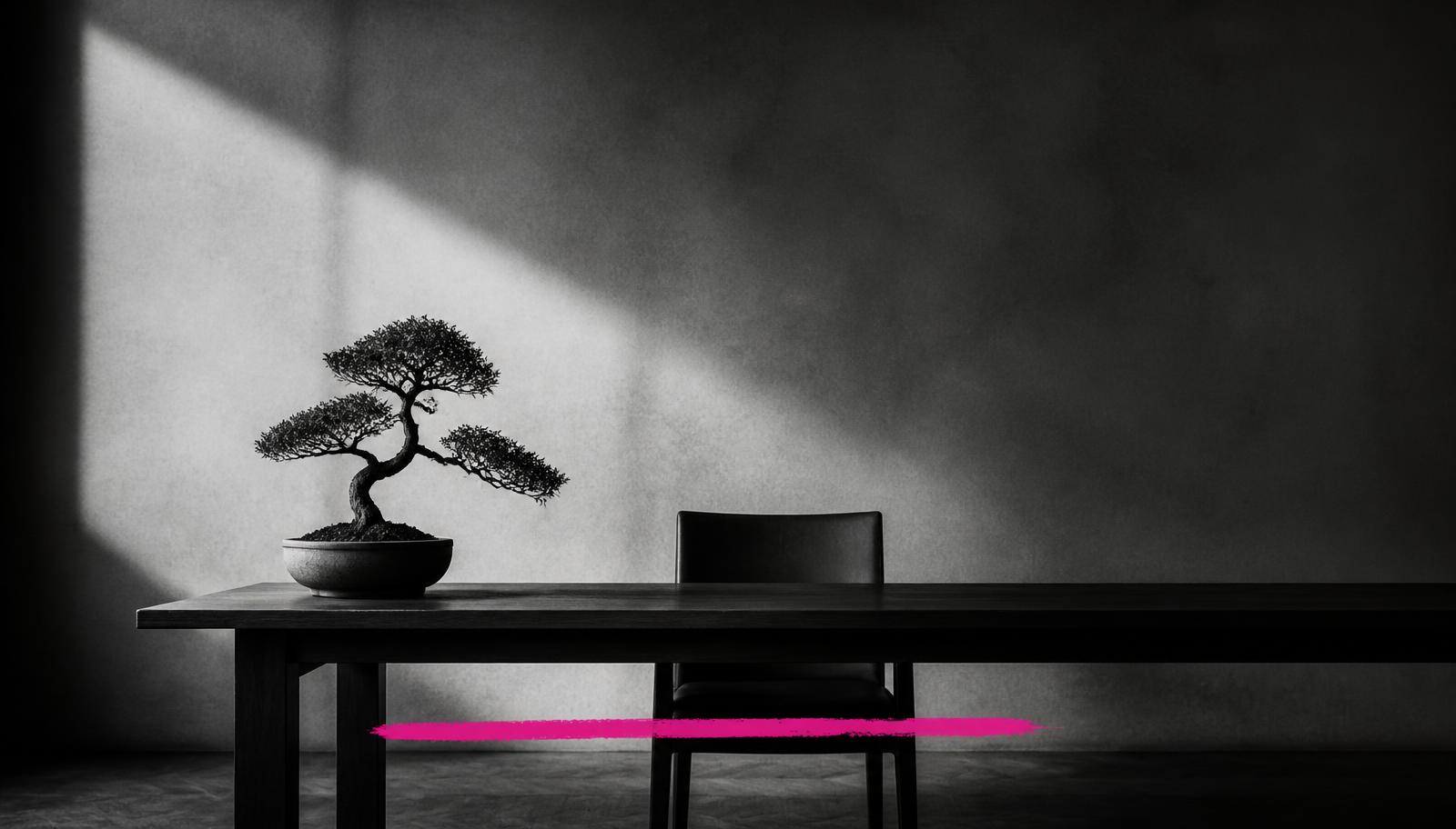 A minimal black-and-white desk with one small potted tree and a single chair, marked by one magenta brush stroke.